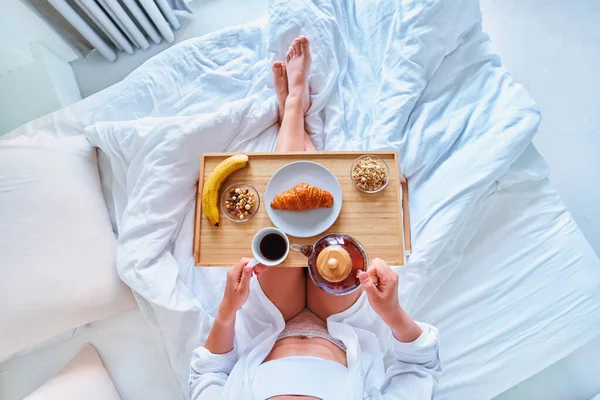 目覚めの女性は快適な怠惰な居心地の良い朝にベッドで朝食をお楽しみください — ストック写真