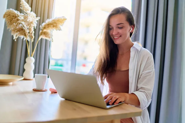 소녀는 집안에서 컴퓨터를 사용하여 현대인 미소짓는 귀여운 소녀를 기뻐하고 — 스톡 사진