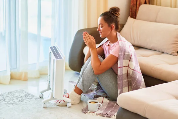 年轻女子 穿着格子呢短袜 坐在家里电热器旁取暖 — 图库照片