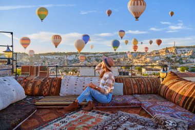 Goreme, Türkiye 'deki güzel varış noktasında, otel terasında kız gezginler tatil yapıyor. Güneş doğarken uçan balonlarla muhteşem Kapadokya, Anadolu