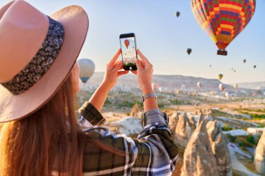 Türkiye 'nin Goreme kentinde kız turist tatilleri. Güneş doğarken muhteşem Kapadokya 'da uçan balonların fotoğrafını çekmek, Anadolu