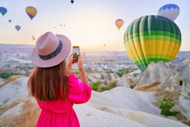 Gezgin kız blogcu Nevsehir, Goreme 'deki manzaralı vadide uçan sıcak hava balonlarının fotoğrafını çekiyor. Anadolu, Kapadokya 'da güzel bir yer