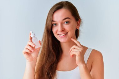 Güzel, sağlıklı bir cilt için elinde serum şişesi tutan çekici genç bir kadının portresi.