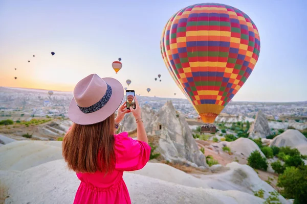 Stock image Girl traveling blogger takes photo on phone camera of flying hot air balloons in scenic valley in Nevsehir, Goreme. Beautiful destination in Anatolia, Kapadokya