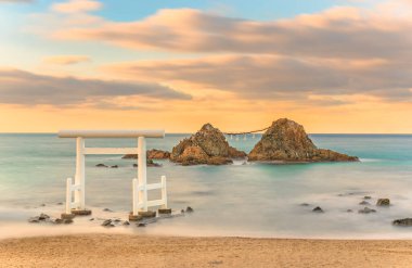 Itoshima Sahili ve ünlü Sakurai Futamigaura 'sı Meoto Iwa Çift Kayalıkları' nın uzun pozlu deniz manzarası akşam günbatımında kutsal beyaz bir Shinto torii kapısı tarafından korunuyor..