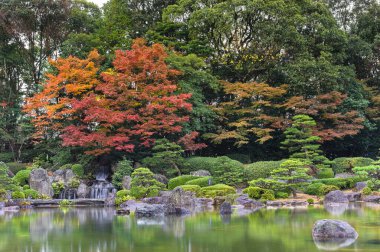 fukuoka, kyushu - Aralık 07 2021: Japon Ohori bahçesinin Ue-no-Ike gölündeki Sandan-Ochi-no-Taki Şelalesini resmeden manzara yağmurda kırmızı momiji akçaağaçlarının sonbahar renkleriyle renklendirilmiş.