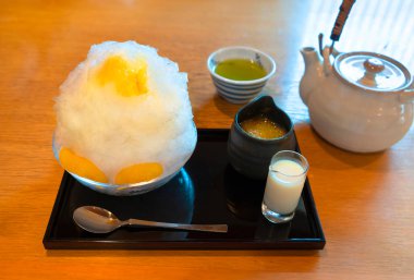 Geleneksel Japon kakigri tıraşlı portakal aromalı buzlu tatlı reçel kabında hamurla dolu ve yoğunlaştırılmış süt ve masada bir çaydanlık yeşil çay..
