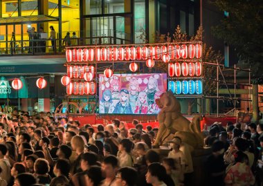tokyo, akihabara - aug 11 2023: Crowd illuminated at night by lanterns aside a broadcast screen displaying manga characters during the Anime Song Bon Odori Dance Festival held in Kanda Myojin Shrine. clipart