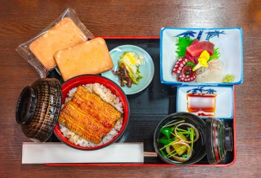 Japon yemeği seti, kabayaki usulü ızgara unagi fileto ile ızgara, üzerine buğulanmış pirinç, ahtapot ve ton balığı sashimi, suimono berrak çorba, fırınlanmış kurabiyeler ve waribashi çubukları.