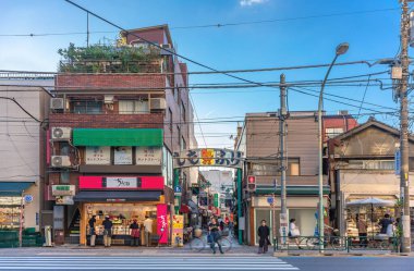 Tokyo, Japonya - Bölüm 17 2023: İnsanlar Shimofuri alışveriş caddesinin girişini işaretleyen büyüleyici maskot Shiichan ile süslenmiş metalik kemerin altında Komagome bölgesinde geziniyorlar.