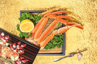 A luxurious seafood feast features fresh crab legs on a bamboo mat accompanied by lemon and parsley set against a golden background with a traditional lacquered Japanese box for gourmet dining image. clipart
