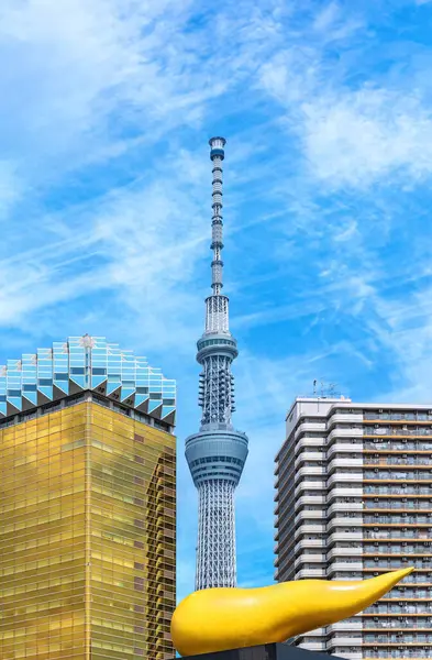 Stock image tokyo, japan - may 17 2024: Japanese Tokyo Skytree tower surrounded by the golden flame sculpture designed by the french designer philippe starck aside the Asahi Beer Headquarter Building in Asakusa.