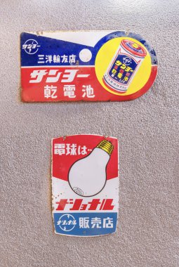 osaka, umeda - dec 05 2024: SanyO Electric tarafından üretilen kuru hücre pilleri için eski Japon paslı emaye tabelaları ve National showcasing retro illustrations and text on a wall.