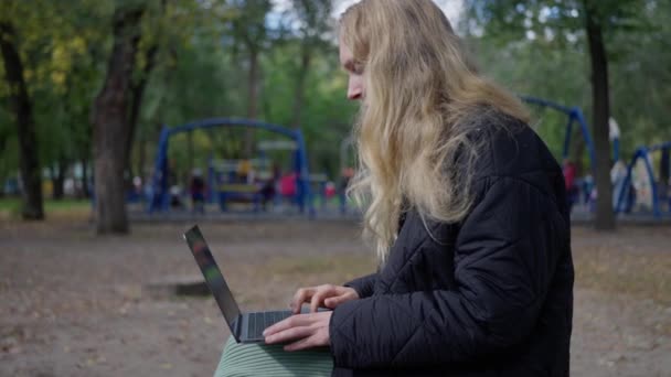 Bilişimci Bir Kadın Sonbaharda Parktaki Bir Bankta Dizüstü Bilgisayarda Çalışıyor — Stok video
