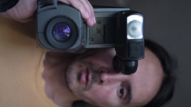 古いビデオカメラを持つ男の肖像画 レトロなビデオカメラの遅い動きを持つハンサムなカメラマン 垂直方向のビュー 高品質4K映像 — ストック動画