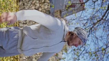 Adam antrenmandan önce ısınıyor, hazırlanıyor, sonbahar bahçesinde kollarını açıyor. Ağır çekim. dikey görünüm