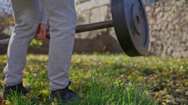 Bir elinde 15 kg halter taşıyan ve sonbahar parkındaki halterin üzerine koyup antrenman için ekipman hazırlayan yakın plan bir vücut geliştirici. Spor konsepti. Yüksek kalite 4k görüntü
