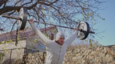 Yakışıklı kaslı adam, sonbahar parkında spor salonunda halterle egzersiz yapıyor. Yüksek kalite 4k görüntü