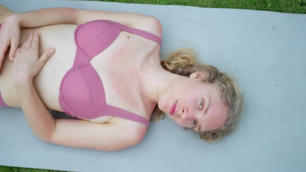 アルビーノの女性は ピンクの水着で ヨガマットに横たわって 芝生の上で ワークアウト スローモーションの後に休んでいる アルビニズム高品質4K映像 — ストック動画