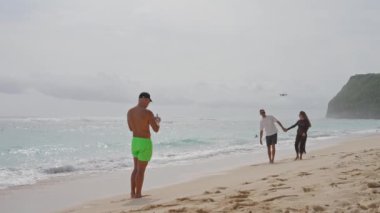 Bali, Şubat 05, 2023 Güzel okyanus kıyısı, bir adam bir drone 'u kontrol ediyor, bir çift sevgiliyi drone kamerasında çekiyor, bir adam ve hamile bir kadın kumsalda el ele yürüyorlar..