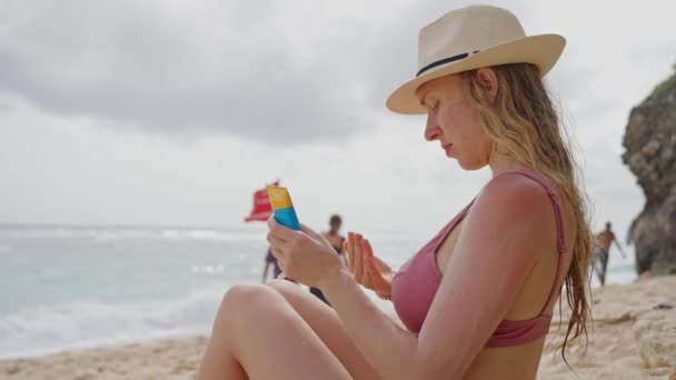 暑い夏の天候での太陽の保護とスキンケア 海で太陽の下でリラックスした晴れた日を楽しむわら帽子の大人の女の子は 休暇中に太陽クリームで自分自身を汚れます スローモーション — ストック動画