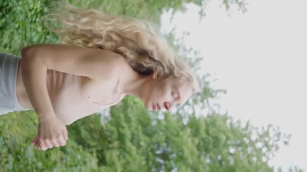 女性選手 長いブロンドの髪 朝のジョギングで 森の中の道路上で スローモーションを実行している 高品質4K映像 垂直ビデオ — ストック動画