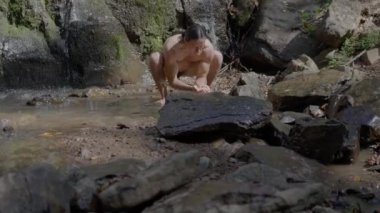 Çıplak gövdeli bir erkek atlet, yüzme şortuyla kendini bir dağ nehrinde yıkıyor. Ağır çekim. Yüksek kalite 4k görüntü