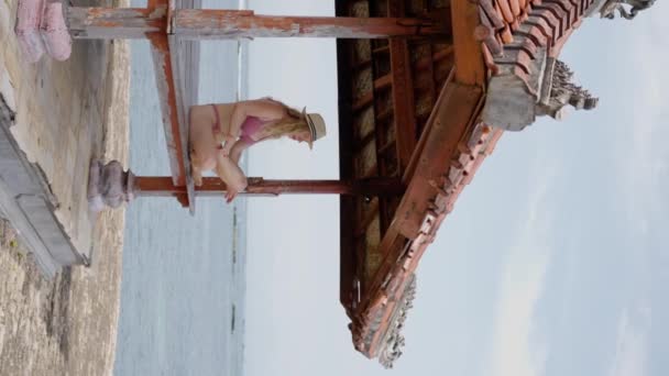 海側の水着のブロンドの女性は 典型的なヨガエリアで瞑想します スローモーション 垂直ビデオ — ストック動画