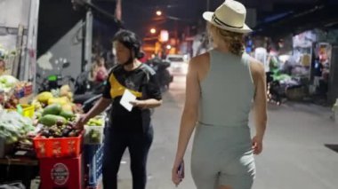 Bali, Endonezya. 23 Şubat 2023. Mavi şortlu ve hasır şapkalı güzel bir kadın turist Asya 'da balık pazarında yürüyor, deniz ürünleri seçiyor. Yüksek kalite 4k görüntü
