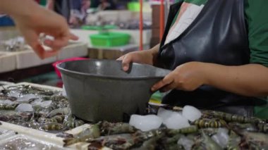 Yeşil tişörtlü ve siyah önlüklü bir kadın marketteki müşteriye taze karides satıyor. 4k video.