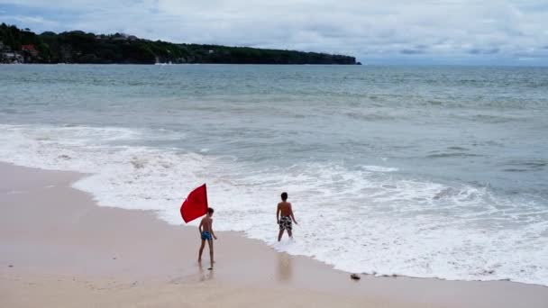 若い男たちは海の海岸に赤い旗の横に署名を禁止水泳として設定を歩く スローモーション — ストック動画