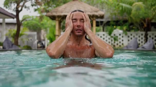 ロングブラックヘア プールの青い水の中に外で泳いでハンサムな白人男性のスローモールクローズアップ肖像画 高品質4K映像 — ストック動画