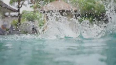 Havuza atlayan ve berrak su sıçratan genç adamın detaylı görüntüsü. Otelin havzasında suyun altında yüzen tanınmayan bir sporcu. Yaz tatilinde dinleniyorum. Yavaş çekim. Yakın çekim.