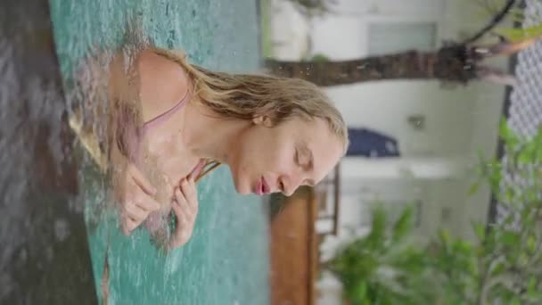 年轻的金发姑娘 在雨中的室外游泳池里游泳的时候 开心地微笑着 一个女人的肖像被拍了下来 垂直的观点 慢动作高质量的4K镜头 — 图库视频影像