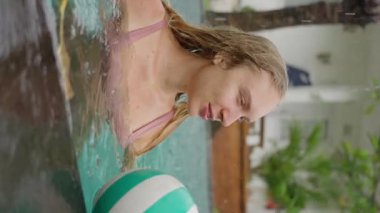 Genç sarışın kız, mutlu ve güler yüzlü, açık havuzda yağmurda yüzerken, bir kadının portresini çekerken. Dikey görünüm. Ağır çekim. Yüksek kalite 4k görüntü