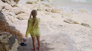Sarı şortlu ve tişörtlü bir turist telefonla video çekiyor, sarışın bir kızın arkasından çekilen görüntü Bali 'nin okyanusunu ve doğasını gösteriyor. Yüksek kalite 4k görüntü