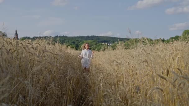 白いドレスを着た美しいウクライナの女の子が小麦畑を走り 背景には青い空があります スローモーション — ストック動画