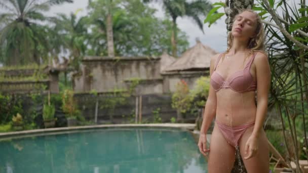 巴厘岛的热带雨林 一位美丽性感的金发女人穿着粉色泳衣站在夏日的淋浴下 慢动作高质量的4K镜头 — 图库视频影像