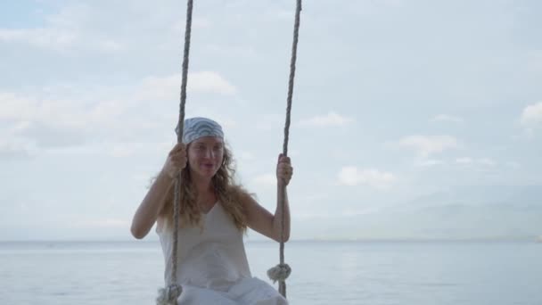 女性スイングライドホリデーバケーションアドベンチャー旅行 女性は海のトリップリゾートで素晴らしい時間を過ごしています ギリ島でリラックス 白いドレスでロマンチックな遊び心のある少女 リゾート ビーチ スローモーション — ストック動画