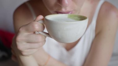 Elinde kahve fincanı olan bir kadın, yeşil bir matcha latte içiyor, ağır çekimde. Yakın plan. Sıcak yeşil çay içeceği. Yüksek kalite 4k görüntü