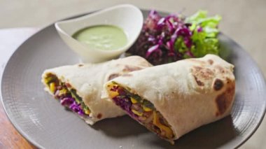 Sebze, mısır, lahanaya sarılmış pide ekmeği. Yanında avokado bazlı yeşil soslu bir fincan tabağı var. Vegan Shawarma. Kapatın. Ağır çekim. Yüksek kalite 4k görüntü