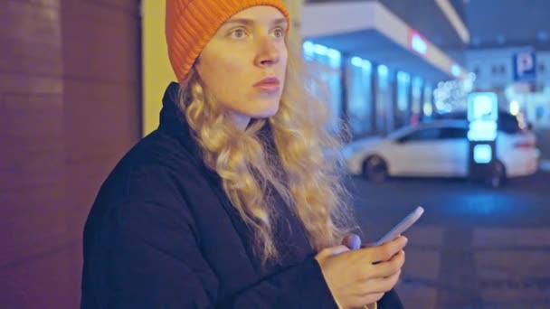 Γυναίκα Πορτοκαλί Καπέλο Και Ένα Μαύρο Μπουφάν Στέκεται Στο Δρόμο — Αρχείο Βίντεο