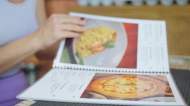 Restoran menüsü okuyan kadın. Yakın plan. Asya kafe 'sinde menüyü tutan kadın yemek ve içecekleri seçiyor. Serinletici ve içecek topluyorum. Seçiyorum. Yavaş çekim