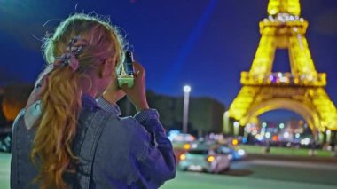 Bir kadın telefonuyla Eyfel Kulesi 'ni çekiyor. Geceleri Eyfel Kulesi çok güzel parlıyor. Sonbahar Paris, Fransa, Yüksek kalite 4K görüntü