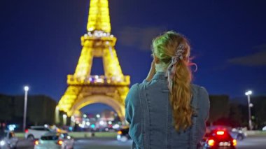 Bir kadın telefonuyla Eyfel Kulesi 'ni çekiyor. Geceleri Eyfel Kulesi çok güzel parlıyor. Sonbahar Paris, Fransa, 04.03.2023. Yüksek kalite 4k görüntü