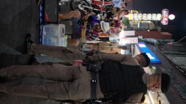 チャイナタウンのナイトストリート アジアのストリートミュージシャンは 歩道の真ん中に夜に演奏 タイ警察は犯人の隣に立っています バンコク 2023 垂直ビュー 4Kについて — ストック動画
