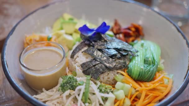 健康的色拉与鳄梨胡萝卜蔬菜和米装饰蓝色的花在木制桌子上 慢动作俯瞰 高质量的4K镜头 — 图库视频影像