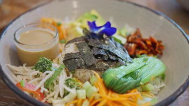 Avokado havuçlu sağlıklı salata sebzeler ve ahşap bir masada mavi çiçeklerle süslenmiş pirinç. Yavaş çekim üst görünümü. Yüksek kalite 4k görüntü