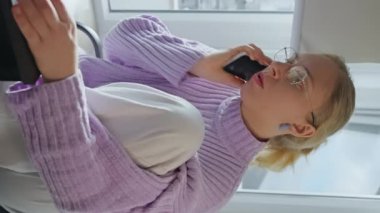 Genç iş kadını telefonda dizüstü bilgisayarla konuşuyor ofis masasında oturuyor, bayan müşteri internet sitesinden alışveriş siparişi konseptini doğrulamak için cep telefonu görüşmesi yapıyor. Dikey görünüm. 4k
