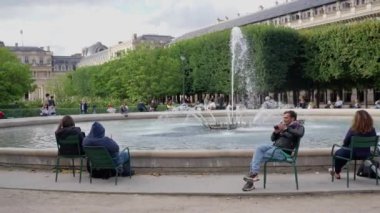 Louvre parkındaki çeşmenin yanında genç insanlar sıcak bir sonbahar gününün tadını çıkarıyorlar. Yüksek kalite 4k görüntü.